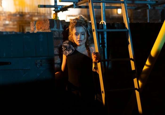 Betsy looks downwards beside some scaffolding in Coronation Street