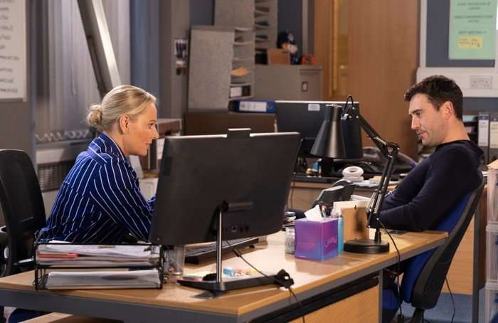 Kit and Lisa sat on opposite sides of a desk in the Coronation Street police station