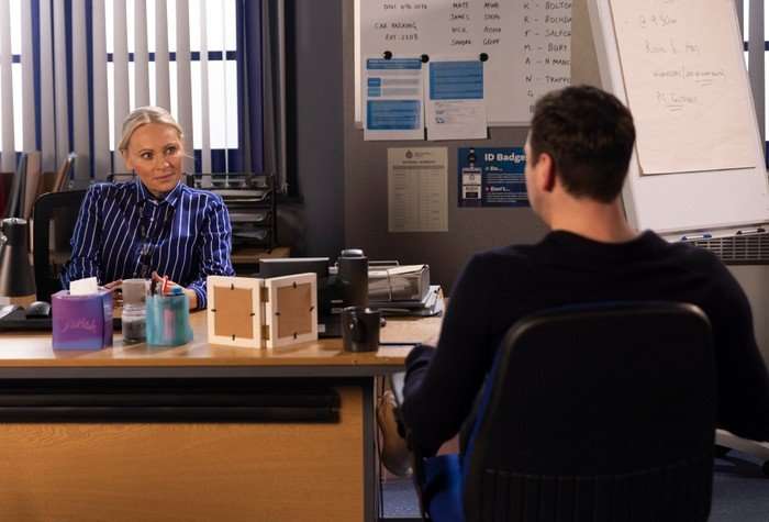 Kit and Lisa sat on opposite sides of a desk in the Coronation Street police station