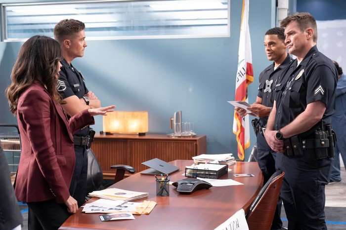 Alyssa Diaz as Angela Lopez, Eric Winter as Tim Bradford, Deric Augustine as Miles Penn and Nathan Fillion as John Nolan in The Rookie, stood around a desk in an office.
