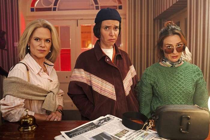 How To Get To Heaven From Belfast (L-R) Sinead Keenan as Robyn Winters, Caoilfhionn Dunne as Dara Friel, Roisin Gallagher as Saoirse Shaw &ndash; they are stood in a row behind a desk, with a newspaper on the table, looking curiously ahead.