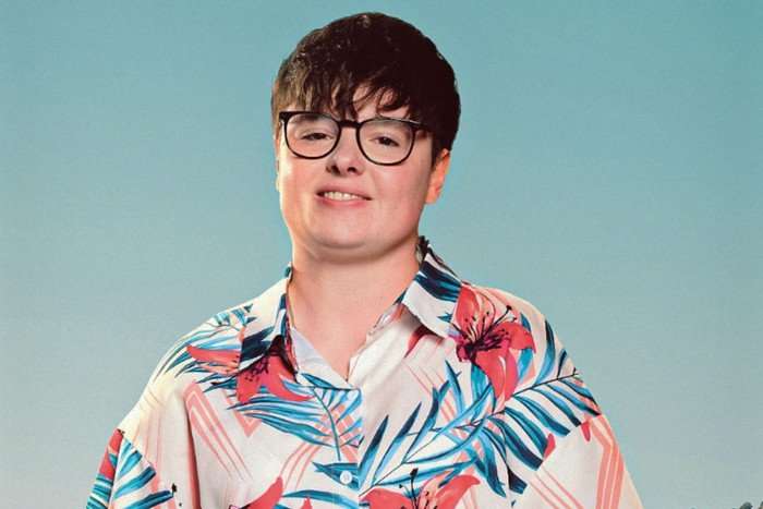 A person is wearing a hawaiian style shirt. they have shortly cropped hair with a long fringe and black glasses