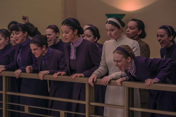 Rowan Blanchard, Mattea Conforti, Chase Infiniti, Lucy Halliday and Isolde Ardies star in The Testaments; a group of young women stand on a balcony looking down at someone and yelling