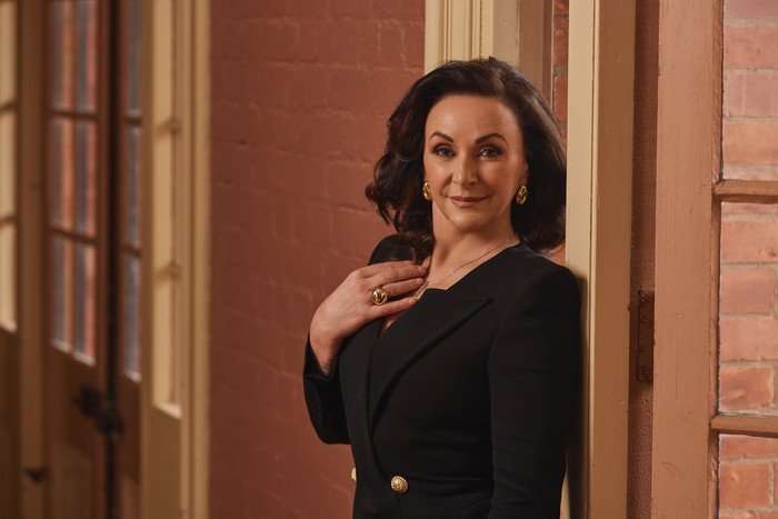 Shirley Ballas resting her back on a wall, posing for a photo. She is looking ahead and resting her hand on her chest.