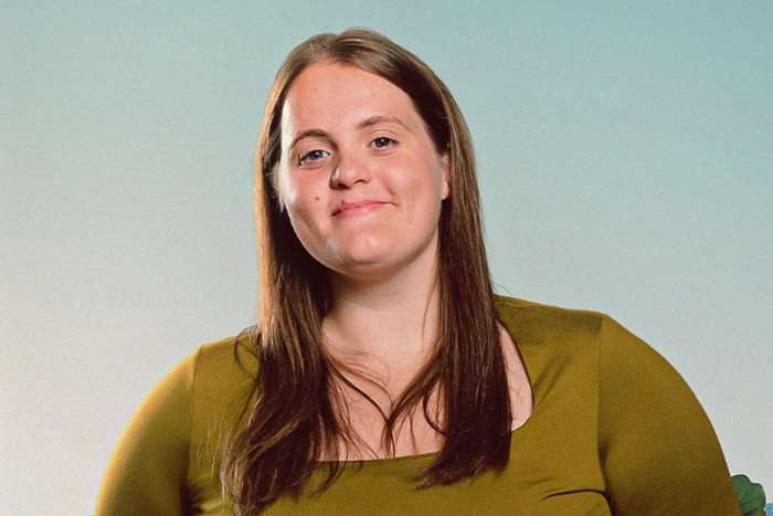 A girl with long brown hair smiles for the camera. She's wearing an olive green top