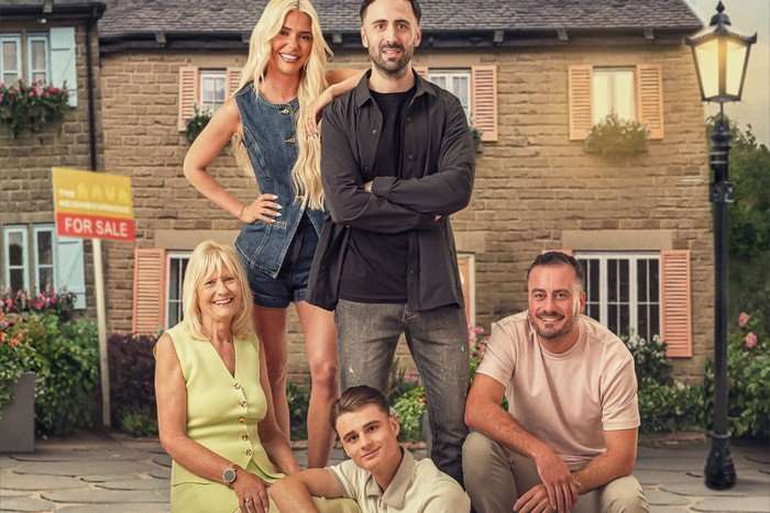 A family of five pose in a town square, smiling for the camera. Alicia, who is blonde and wearing a denim dress, is posing with her arm on Lukas, who is in a black t-shirt and overshirt and has his arms crossed. Fay is on the left, sitting in a lime dress, while Zach leans his arm on her knee. Nathan, in a pink shirt, is crouched on the steps on the right.