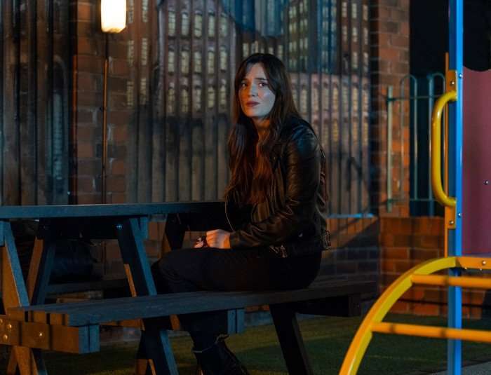 Jodie sits on a bench in the precinct playpark in Coronation Street