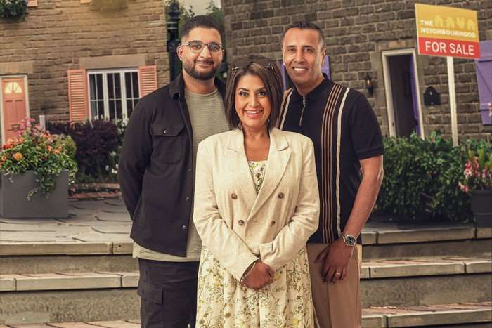 Two men and a woman stand in a town square. The men are standing behind the woman, who is slightly shorter than them. All are smiling for the camera.