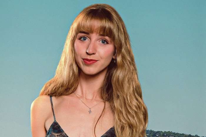 A girl with long strawberry blonde hair poses for the camera. She's got on red lipstick and is wearing a strappy black top