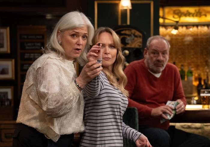 Todd helps Vanessa throw a dart as Jimmy watches on in a scene from Emmerdale