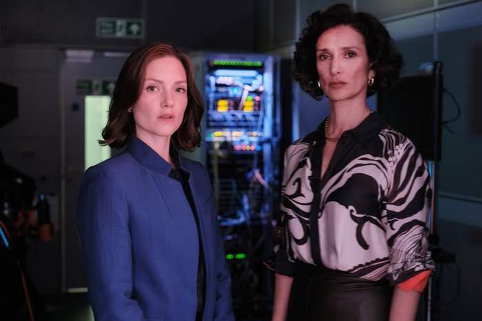 Holliday Grainger as Rachel Carey and Indira Varma as Khadija Khan in The Capture season 3, stood next to each other in front of camera equipment and screens.