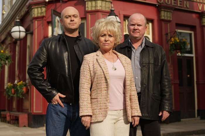 Ross Kemp as Grant Mitchell, Barbara Windsor as Peggy Mitchell, and Steve McFaddden as Phil Mitchell pose in a promo image in front of the Queen Vic pub for EastEnders in 2005.