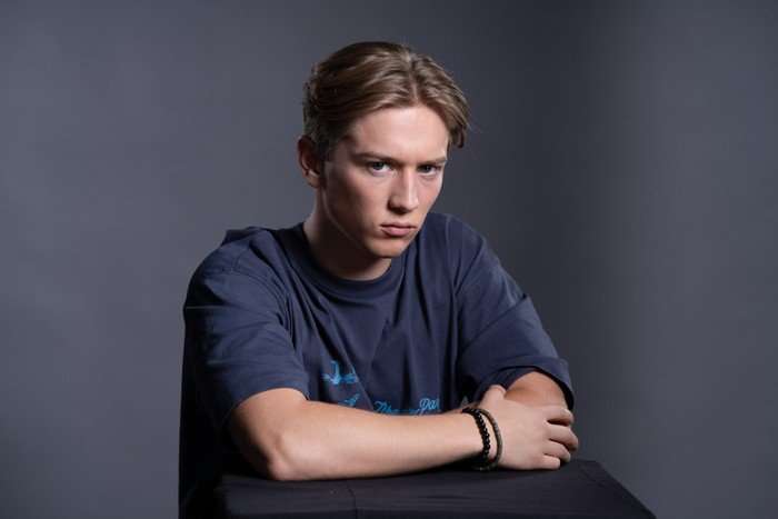 Max Murray sits scowling with his arms folded as Joel Marshall for EastEnders.