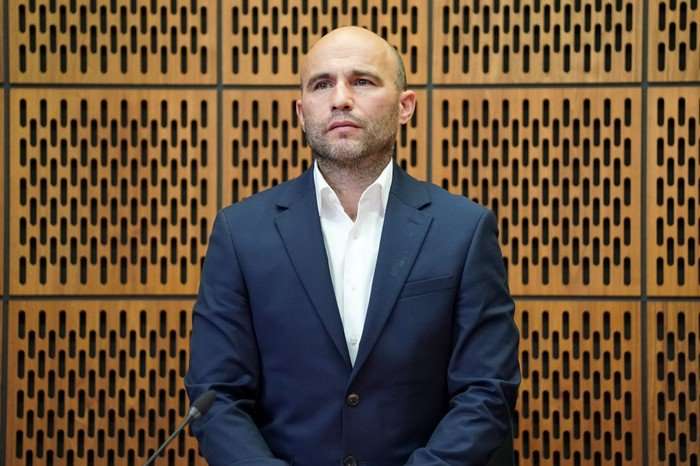 Teddy stands in court in a blue suit in EastEnders