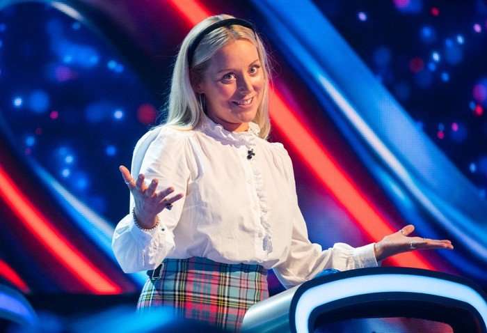 Anna Haugh stood in in front of a podium on The Weakest Link, smiling with her head turned to one side and her arms in the air.