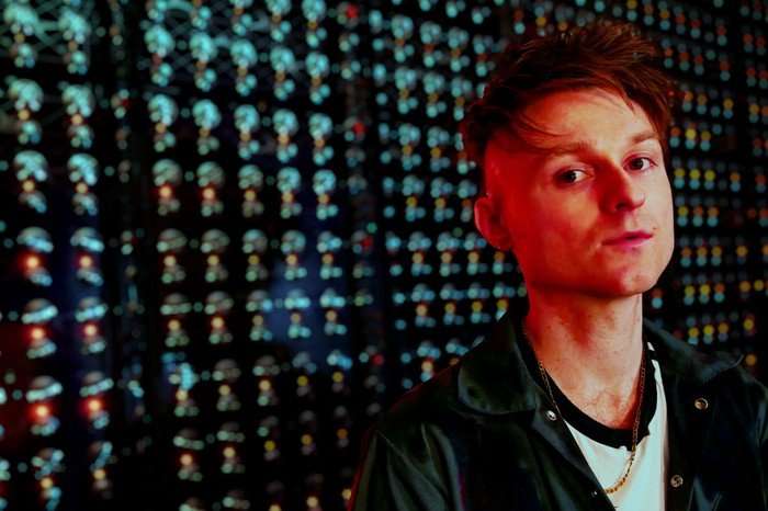 Sam Battle pictured from the side, wearing a blue boiler suit and a white t-shirt.