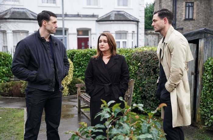 Mark, Vicki and Zack stand awkwardly in the Square Gardens in a scene from EastEnders