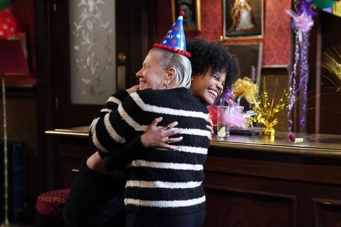 Mo, in a party hat, hugs Jasmine in a scene from EastEnders