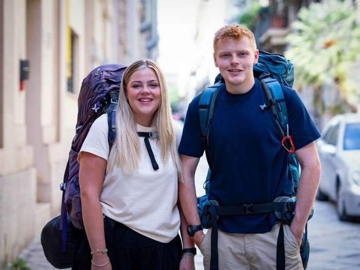 Katie and Harrison stood next to each other smiling ahead with large rucksacks on their back.