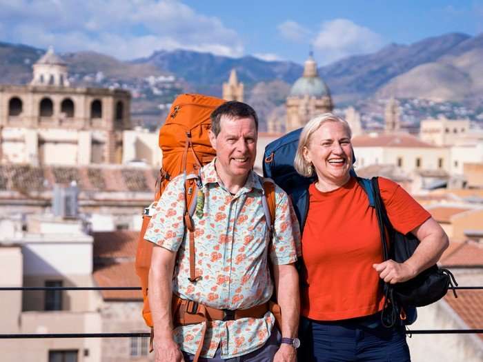 Mark and Margo stood next to each other, smiling ahead as they have large rucksacks on their back.