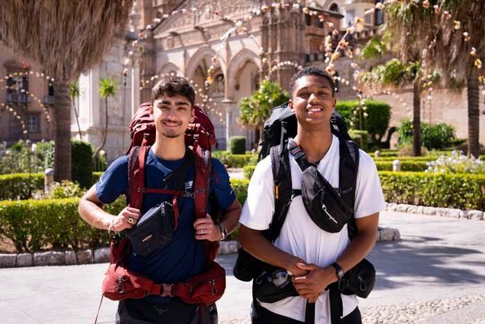 Kush and Jo stood next to each other smiling ahead with large rucksacks on their backs.