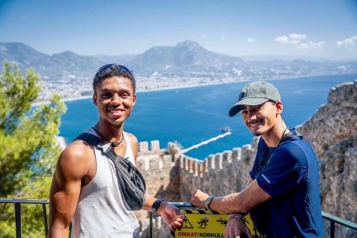 Jo and Kush looking out at sea, smiling ahead as they pose for a photo.