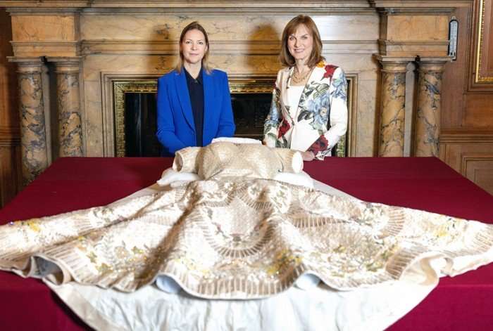 Fiona Bruce and Caroline de Guitaut stood next to one another behind a large red table with the coronation dress laid out.