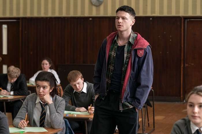 Stuart Campbell as Young Ruben in Half Man, stood in an exam hall, with students in uniform sat around him.