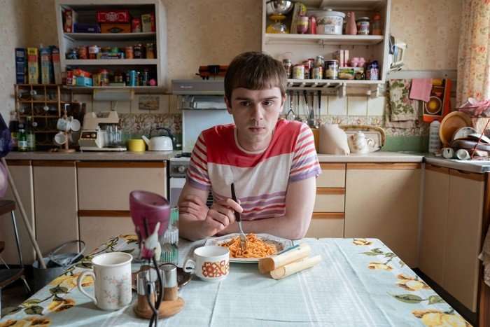 Mitchell Robertson as Young Niall in Half Man, sat at a kitchen table, holding a fork over a plate of spaghetti.
