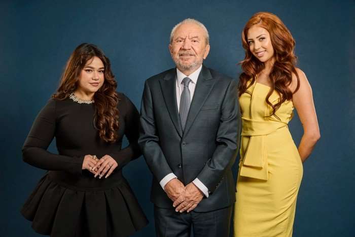 Karishma Vijay, Lord Sugar and Pascha Myhill all stood in business attire smiling ahead in front of a dark blue background.