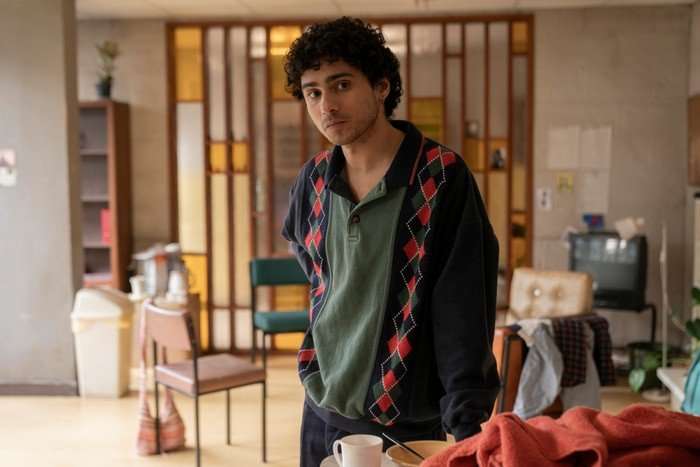 Bilal Hasna as Young Alby in Half Man, wearing a green top and blue jacket and stood in a living room.