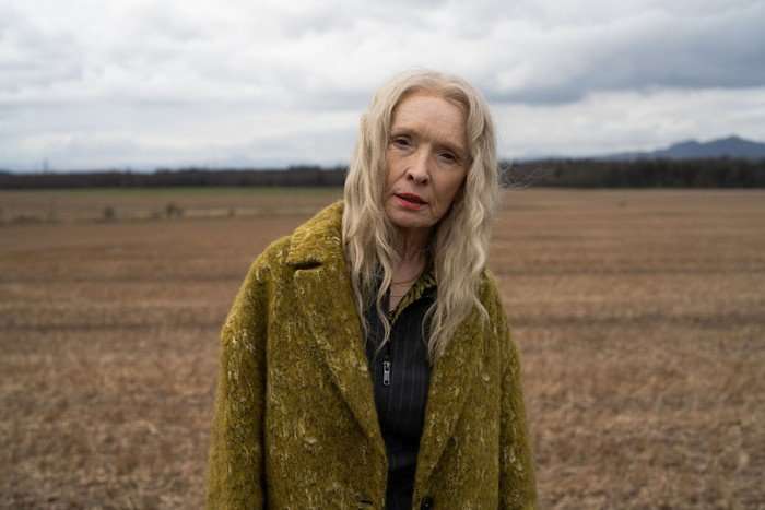 Lindsay Duncan as Ollie in Mint, wearing a yellow/green coat and stood in a field.