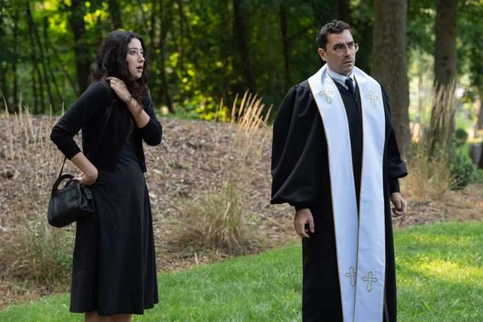 Taylor Ortega as Morgan and Dan Levy as Nicky in Big Mistakes, stood outside, both wearing black and Levy is wearing a white stole.
