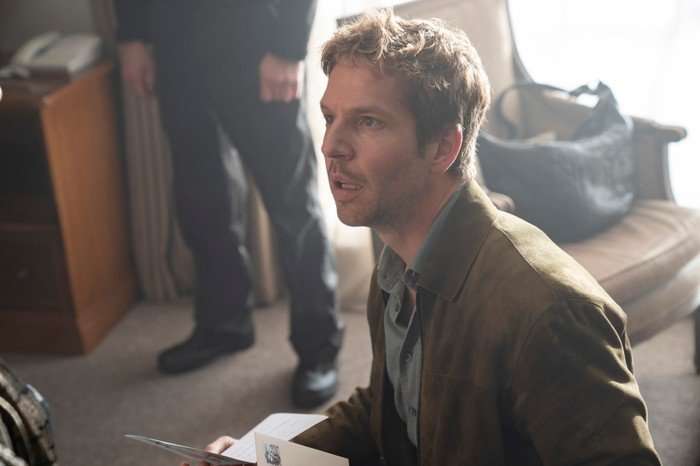 Damien Molony as Jim Bergerac in Bergerac. He wears a brown blazer jacket over a blue shirt and wears a shocked expression.