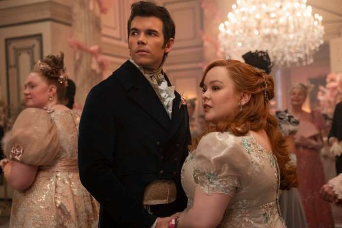 Luke Newton as Colin Bridgerton, Nicola Coughlan as Penelope Bridgerton in Bridgerton standing in the middle of a ball, turning around to look at something.