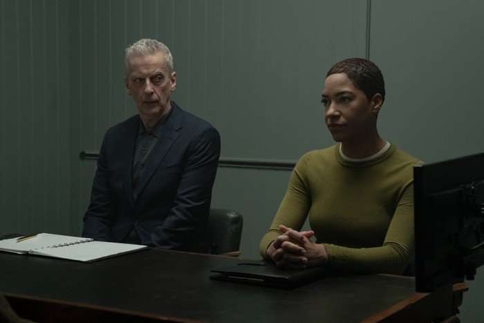 Peter Capaldi as DCI Daniel Hegarty and Cush Jumbo as DS June Lenker in Criminal Record, sat one side of a table in a police interview room.