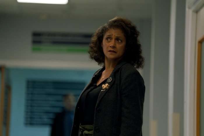 Cathy Tyson in Criminal Record, wearing a black jacket and stood in a corridor.