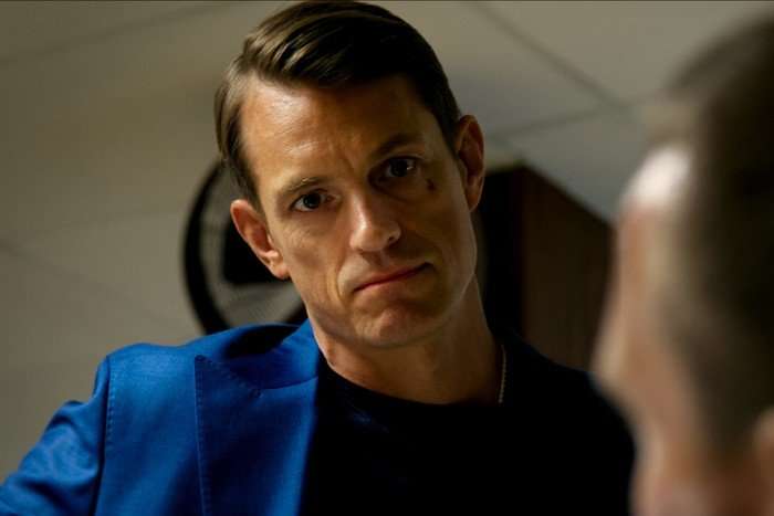 Joel Kinnaman as Tom Waaler in Detective Hole, wearing a blue jacket and looking down at someone, angry.