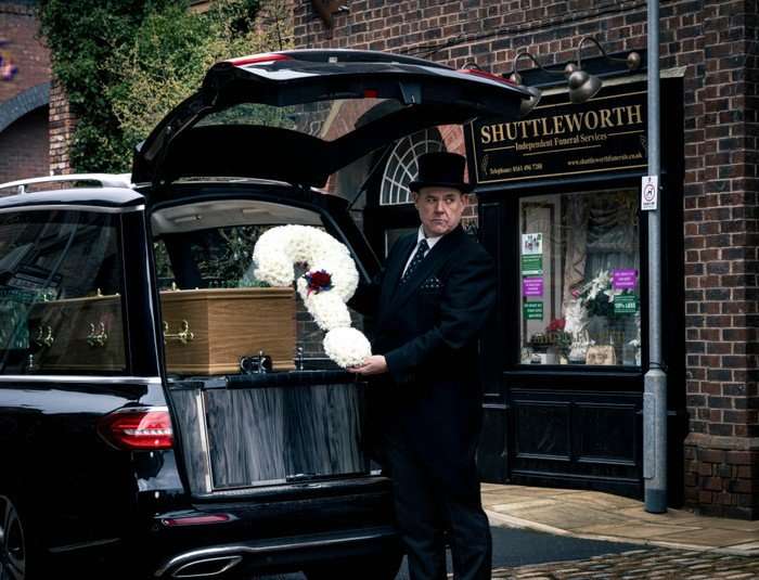 George loads a question mark shaped floral arrangement into the back of a hearse in Coronation Street
