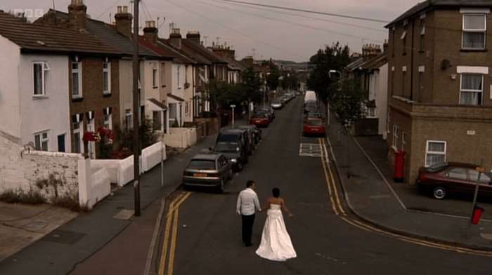 Shane Richie as Alfie Moon and Jessie Wallace as Kat Slater in a wedding dress walk down a street hand in hand in a scene from EastEnders.