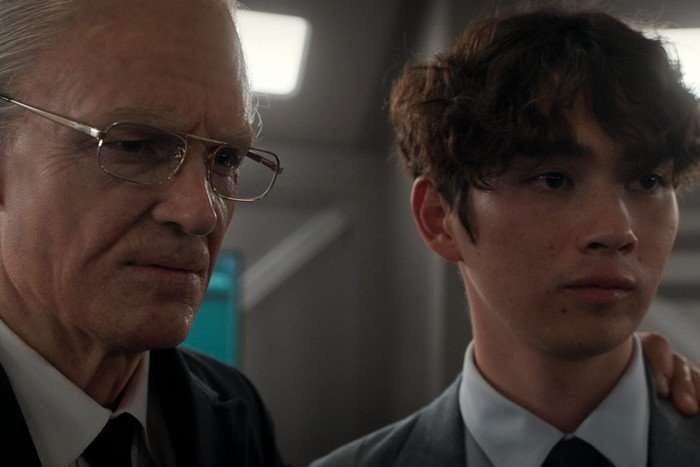 Joel Kinnaman as Ed Baldwin stands beside Sean Kaufman as Alex Poletov, resting a hand on his shoulder, both in suits inside a softly lit spacecraft interior in For All Mankind season 5