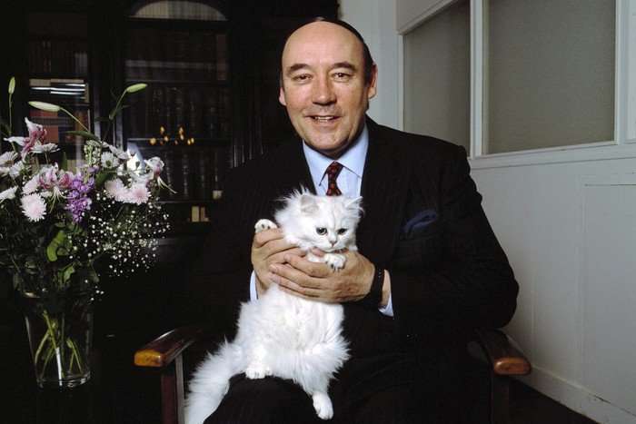 Desmond Morris, wearing a black suit and white shirt, sat down with a white cat in his hands.