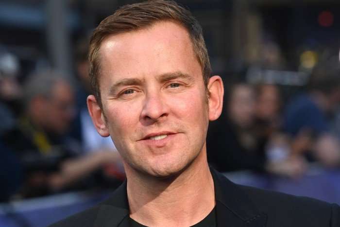 A close up of Scott Mills, smiling ahead as he poses for a photo.