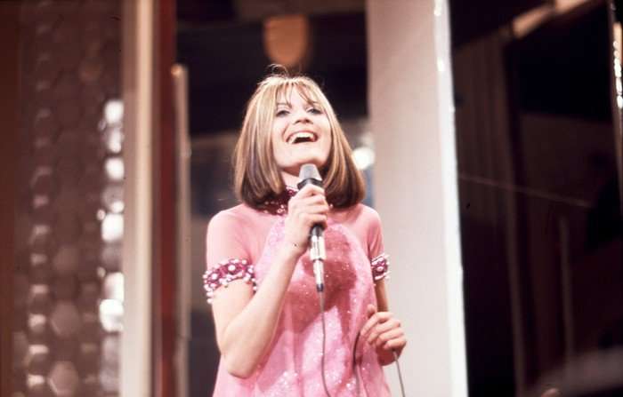 A woman wearing a pink dress, holding a microphone and singing.