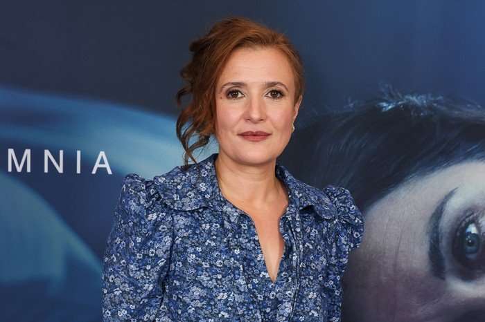 Lyndsey Marshal, wearing a blue dress and stood in front of a blue backdrop.