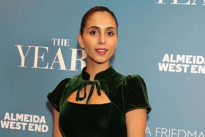Anjli Mohindra, wearing a green dress and stood in front of a blue backdrop.