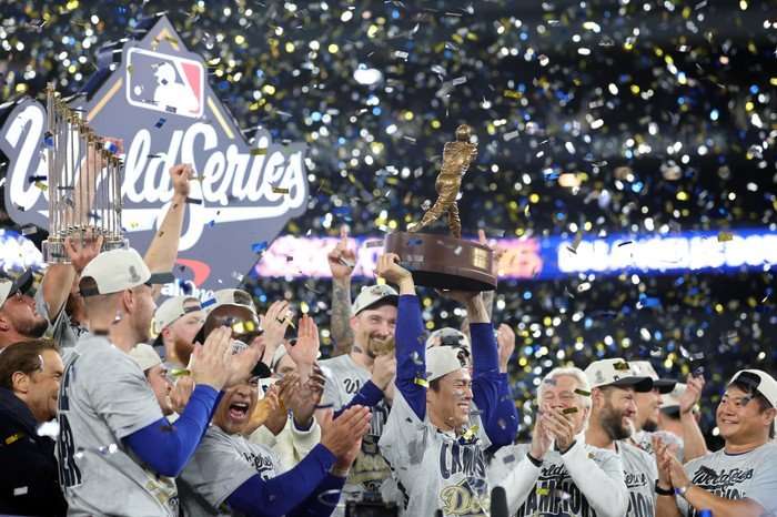 The LA Dodgers celebrate winning the World Series 2025, with the trophy held up in the air and confetti falling.