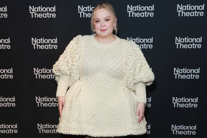 A blonde woman wearing a crochet look cream dress smiles ahead.