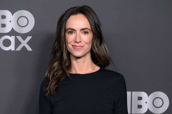 Amy Manson, wearing a black dress, stood in front of a black backdrop.