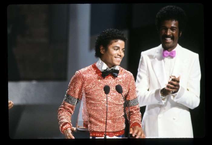 Michael Jackson stood on stage wearing a sparkly red jumper with a black bowtie.